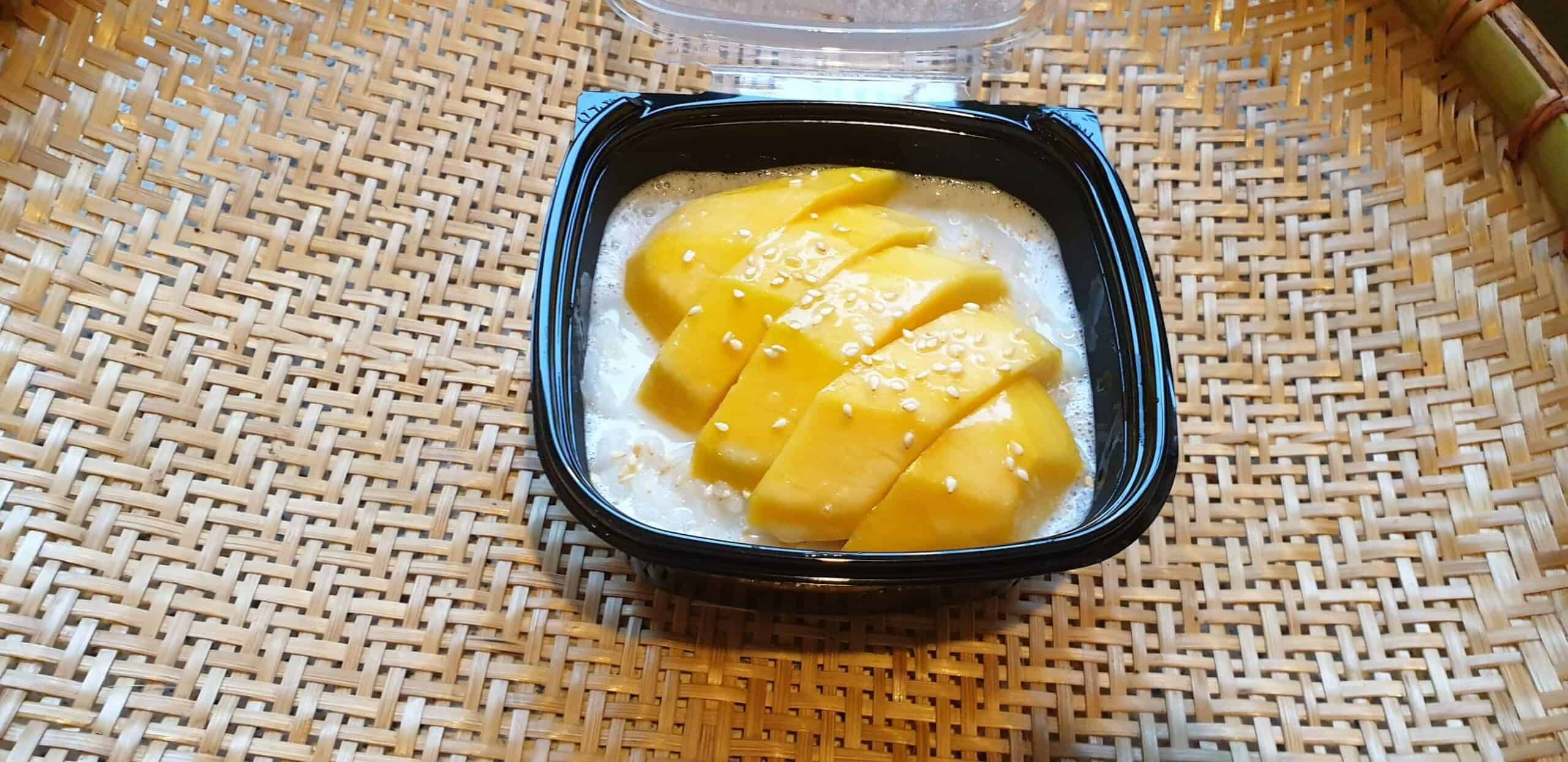 Traditionele Thaise mango sticky rice met kokosmelk in een zwarte kom.