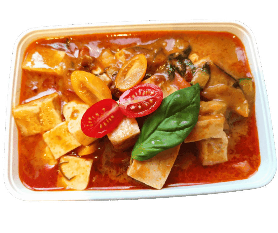 Thaise curry met tofu, tomaat en basilicum in een witte schaal.