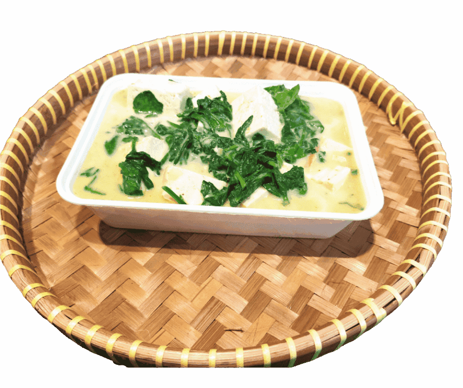 Thai curry met tofu en verse groenten in een witte kom op een rieten dienblad.