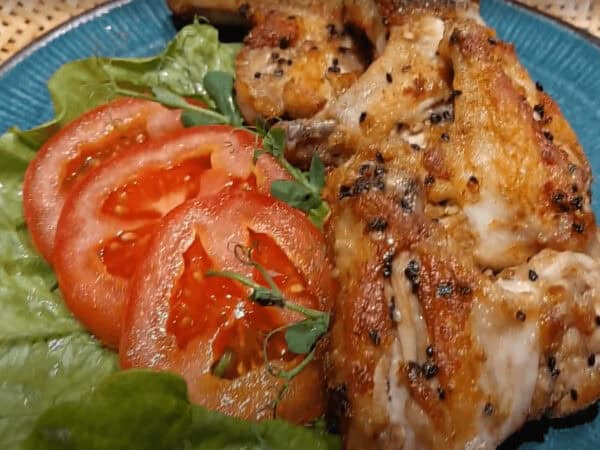 Gegrilde kip met tomaat en sla op een blauwe schaal.