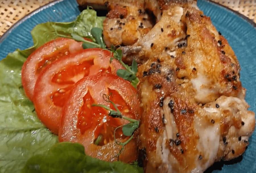 Gegrilde kip met tomaat en sla op een blauwe schaal.